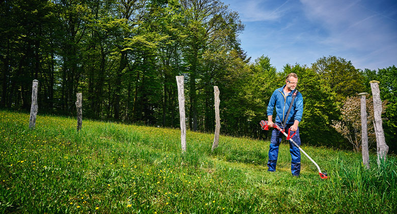 a man is trimming the lawn with a Einhell cordless lawn trimmer