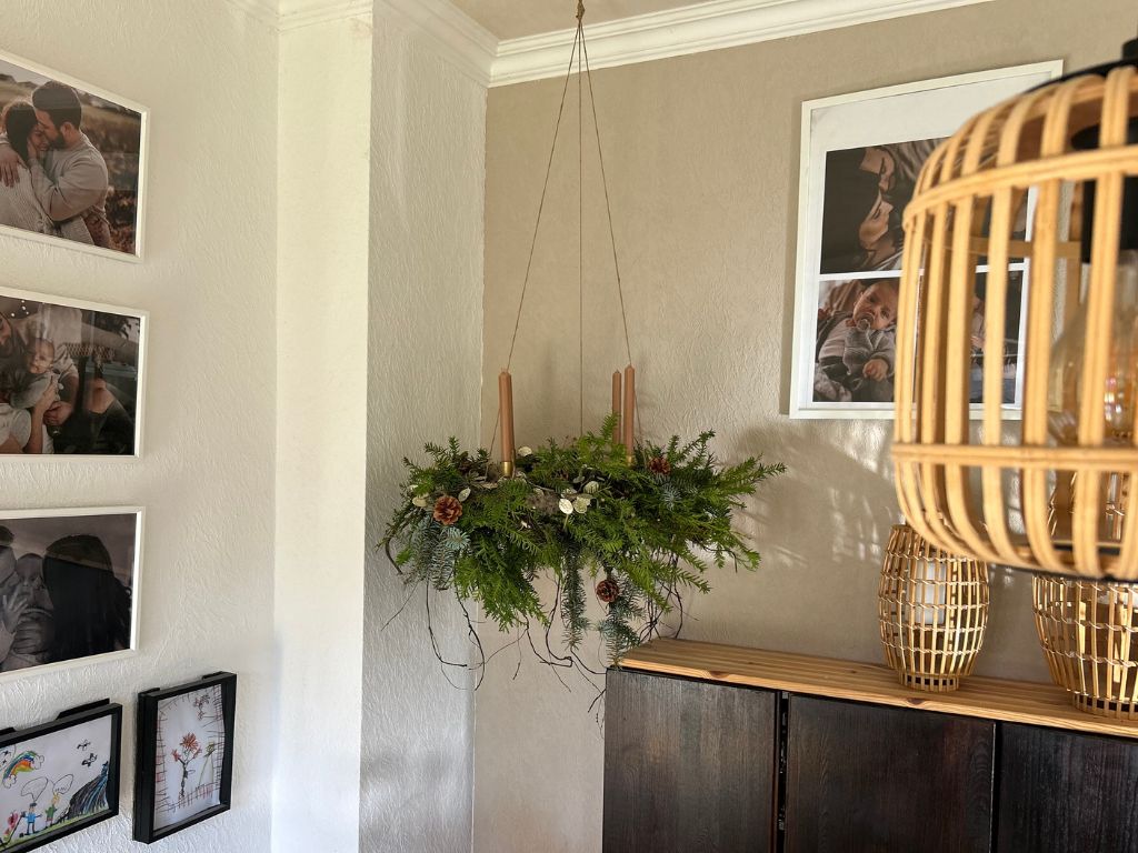 Ein hängender Adventskranz aus Tannengrün mit vier braunen Stabkerzen, verziert mit Zapfen und Trockenpflanzen.