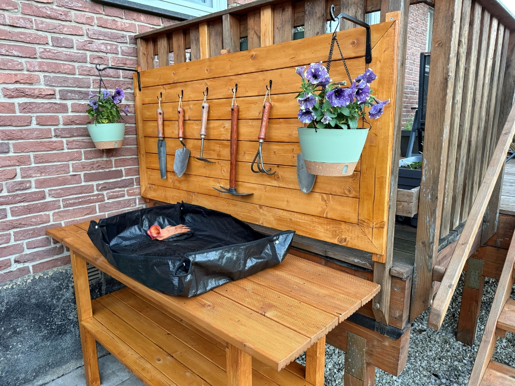 Ein fertig dekorierter Pflanztisch mit Rückwand, Gartenwerkzeugen, Blumenampel und Pflanzunterlage.