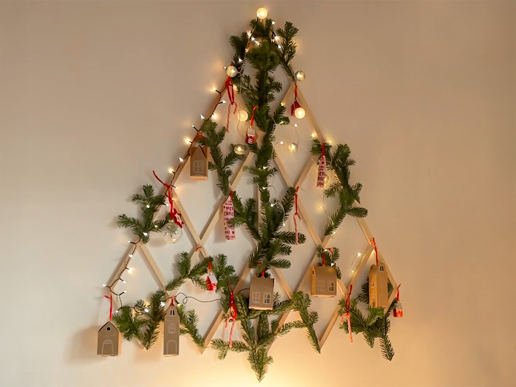 Ein dekorierter DIY-Holz-Weihnachtsbaum in Tannenbaumform mit Lichtern, Tannenzweigen und kleinen Geschenkschachteln.