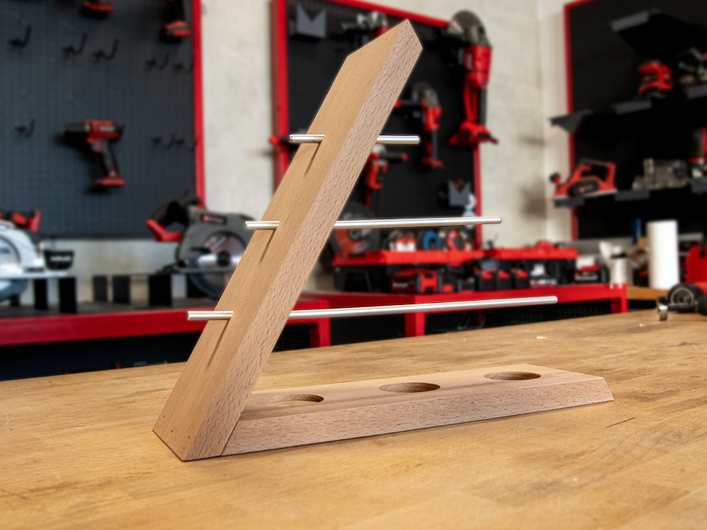 Ein schräg stehender Schmuckständer aus Holz mit vier Metallstangen und drei runden Aussparungen im Sockel.