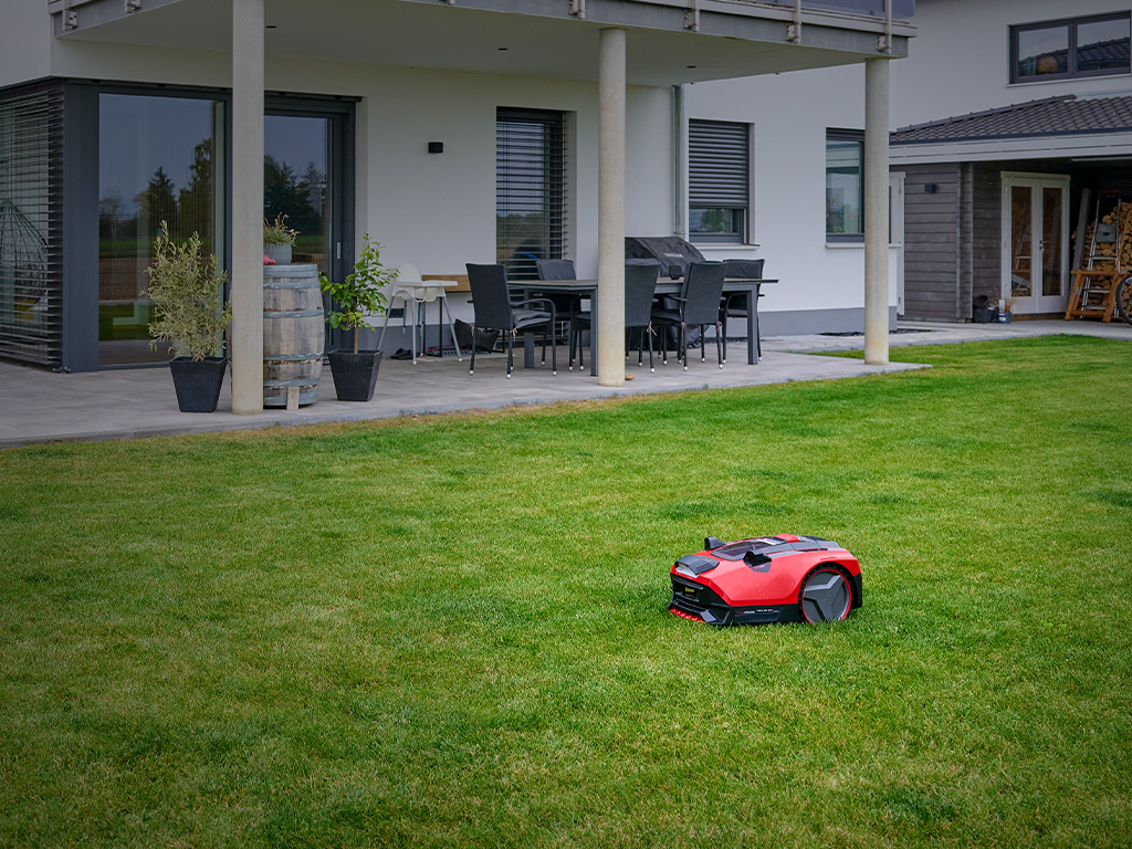Der Einhell Mähroboter FREELEXO CAM fährt auf einer gepflegten Rasenfläche vor einem modernen Haus.