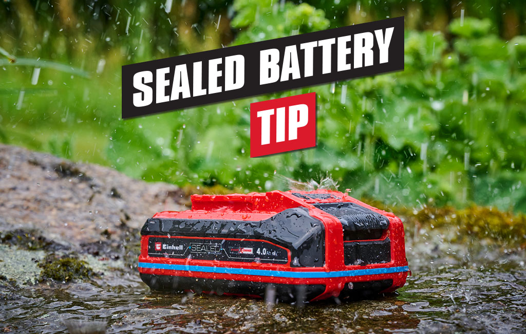 A weatherproof Einhell SEALED rechargeable battery lies on a stone in the rain, with the inscription "Sealed battery tip" in the foreground.