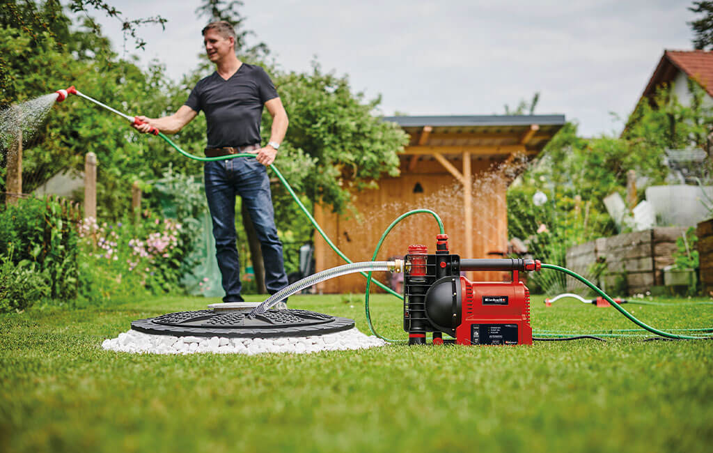 Ein Mann gießt die Blumen in seinem Garten mit Regenwasser und der Hilfe einer Gartenpumpe.