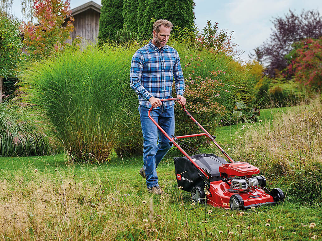 Ein Mann mäht den Rasen in einem Garten mit einem Einhell Rasenmäher