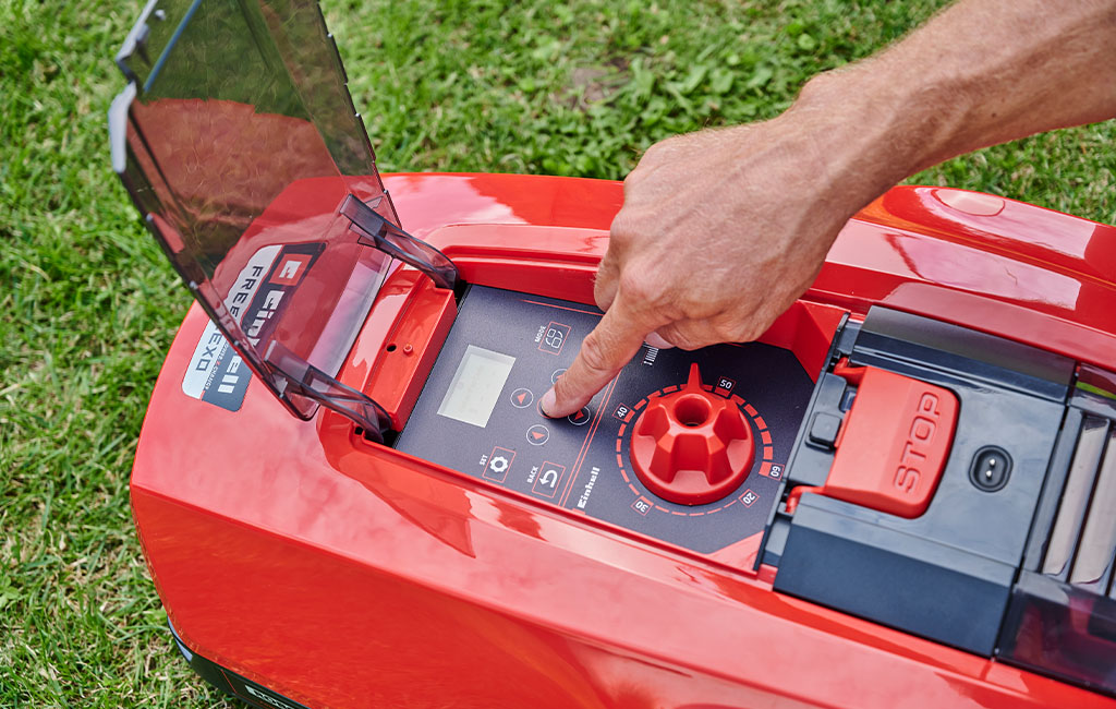 A male hand operating the keypad of a robotic lawnmower.