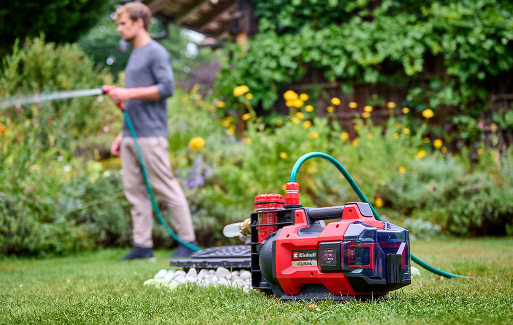 A man waters the garden with a cordless garden pump in the foreground.