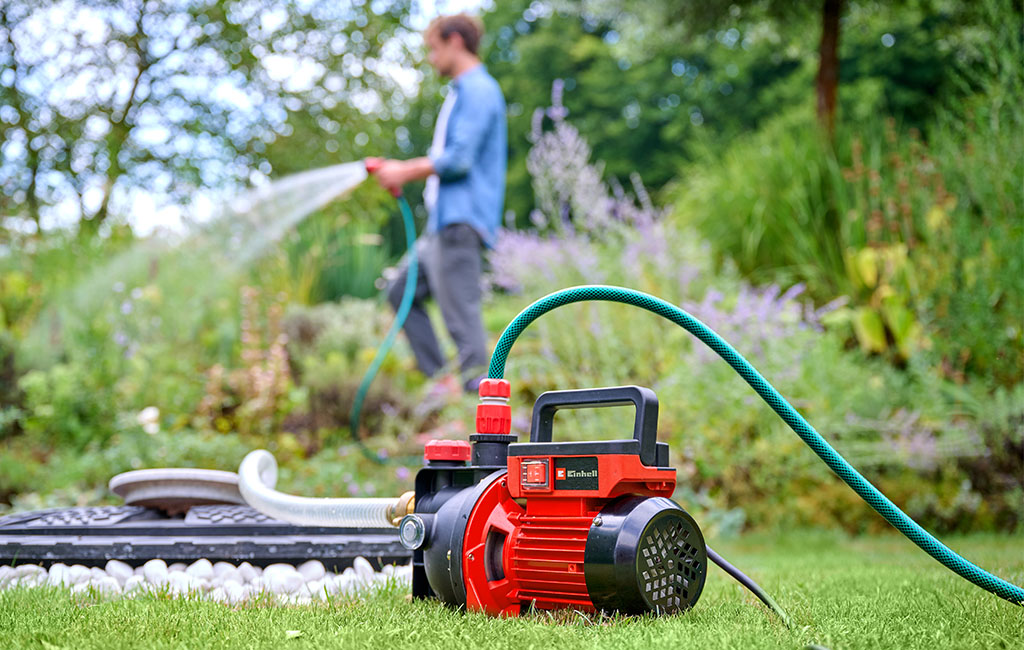 A man waters the garden while a garden pump is visible in the foreground.