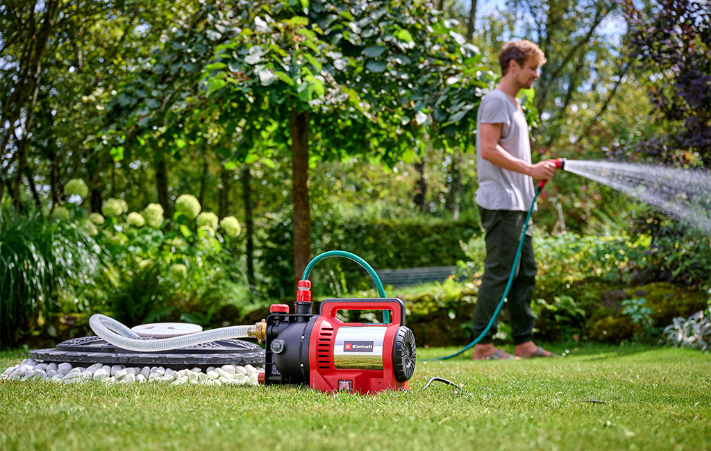 A man waters the garden with a red Einhell garden pump in the foreground.