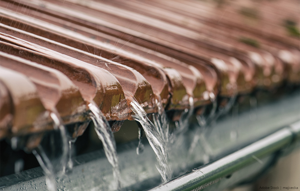 Regenwasser fließt über die Kante von roten Dachziegeln in eine Dachrinne.