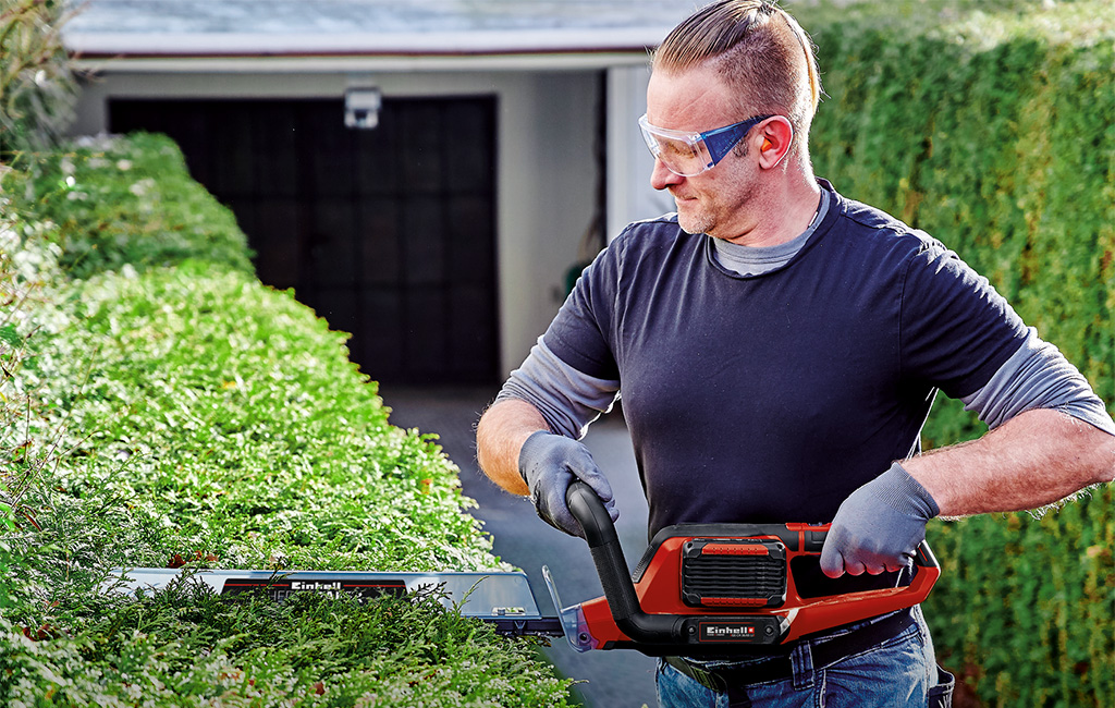 ein Mann schneidet eine Hecke mit einer Einhell Akku-Heckenschere