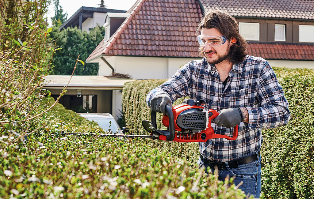 ein Mann schneidet eine Hecke mit einer Einhell Benzin-Heckenschere