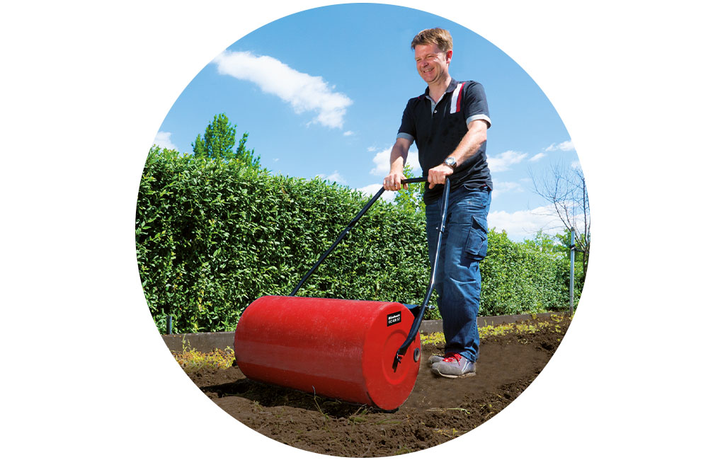 A man rolls the ground with the Einhell lawn roller