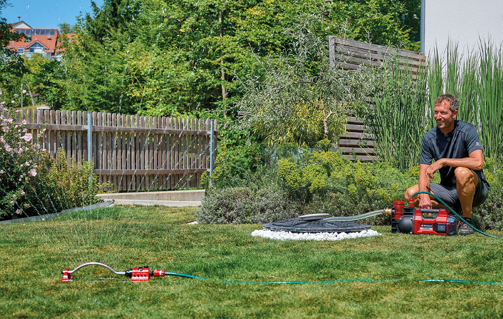 ein Mann wässert den Rasen mithilfe eines Rasensprengers und einer Einhell Akku-Gartenpumpe