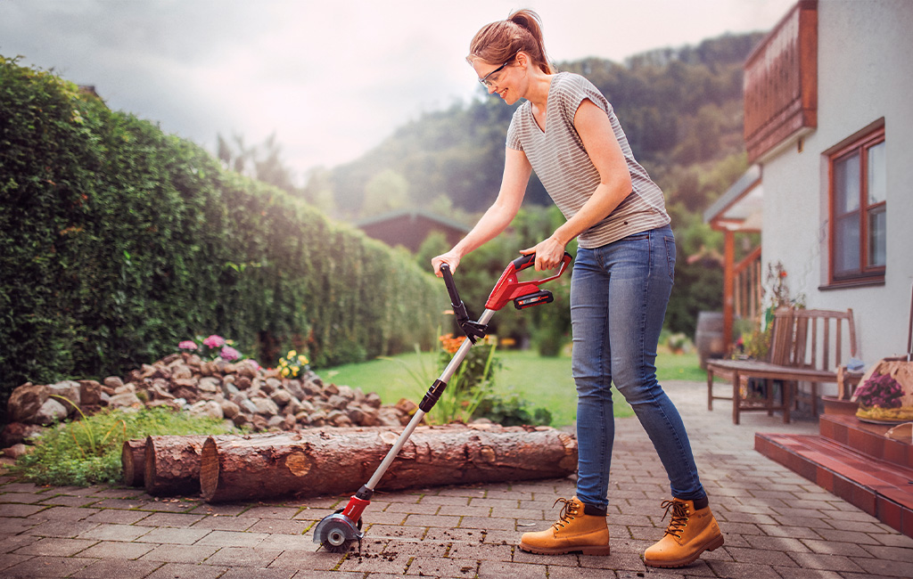 a woman cleans the joints of her paving stones with the Einhell cordless grout cleaner