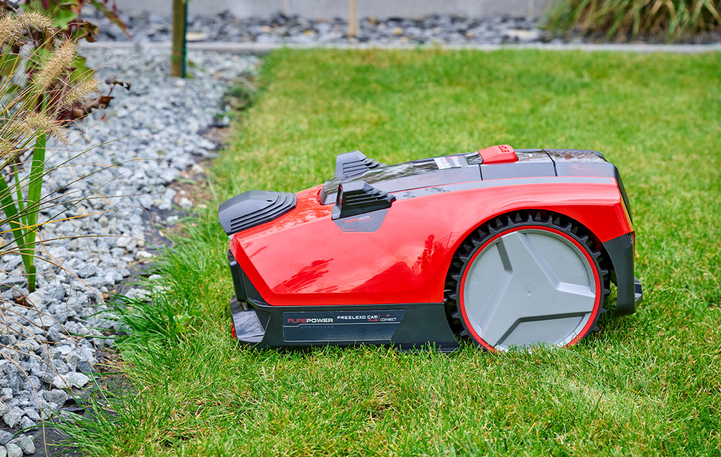 An Einhell Freelexo Cam robot lawn mower in a garden in front of the lawn border.