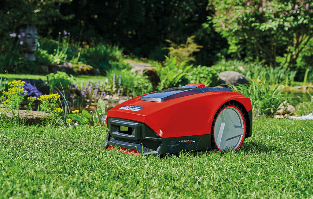 An Einhell Freelexo robot lawn mower in front of a garden pond.