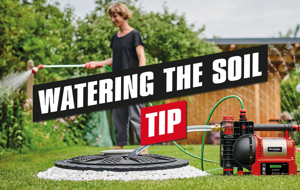 A woman watering her garden with the help of a garden pump. The text in de picture says: Watering the soil - Tip.