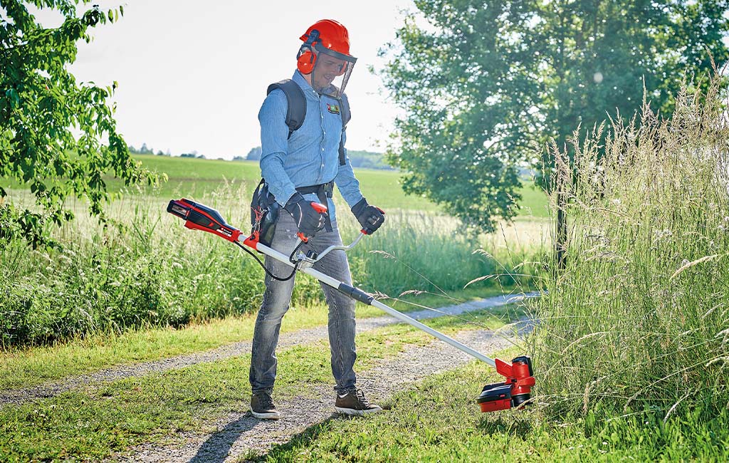 Ein Mann mit Schutzkleidung beim Mähen eines Wegrandes mit einer Akku-Motorsense.