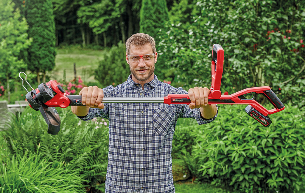 ein Mann hält einen Einhell Akku-Rasentrimmer in die Höhe