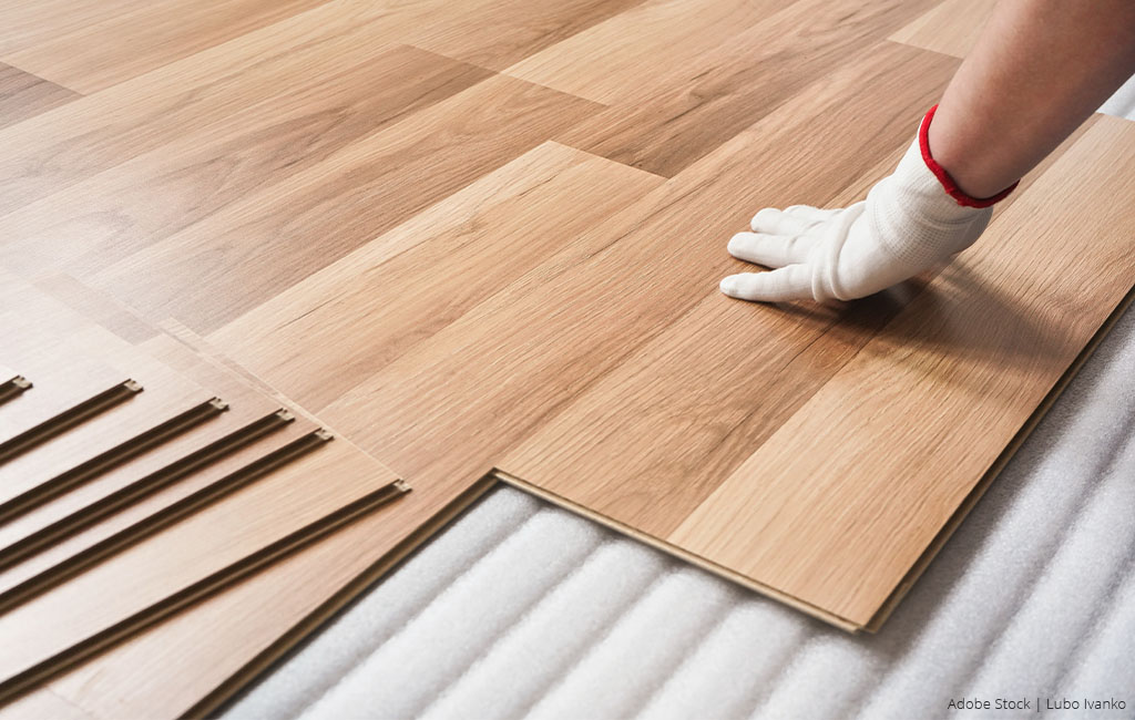 A person wearing gloves is installing wooden flooring in a room.