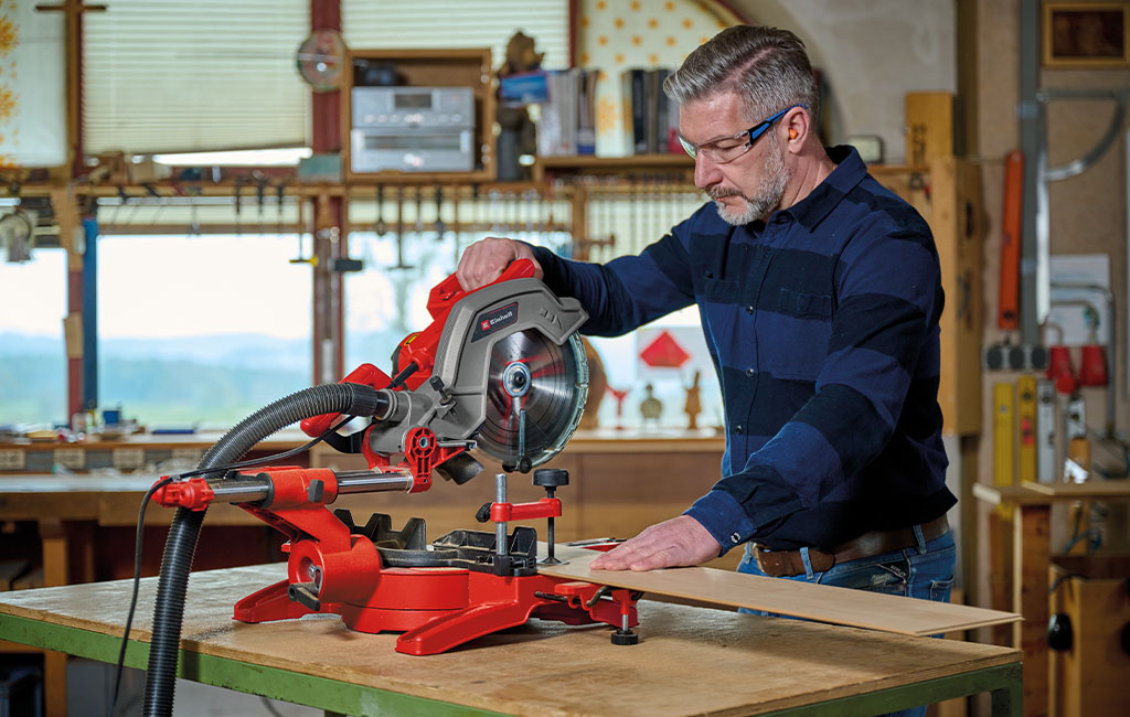 A man using an Einhell miter saw to cut wooden planks.