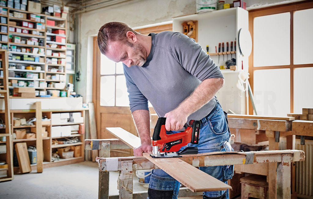 A man cutting wood with an Einhell jigsaw in a workshop.