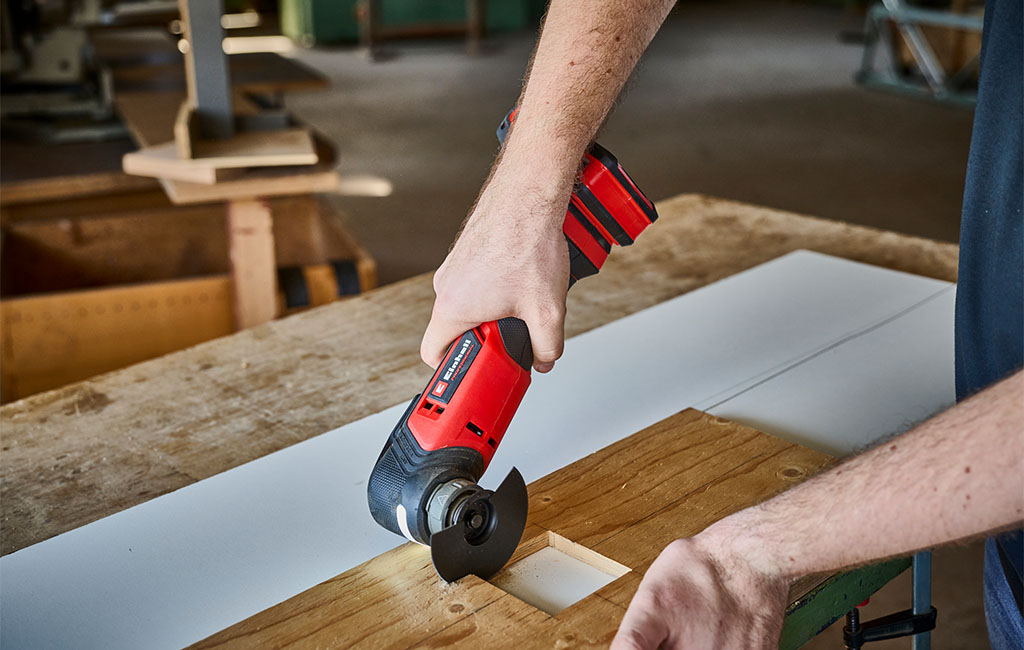 A hand holding an Einhell cordless multitool to work on wood.