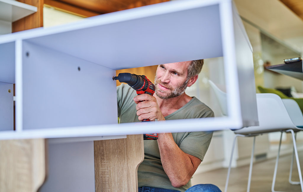 A man fastens a screw to a piece of furniture using an Einhell cordless drill.