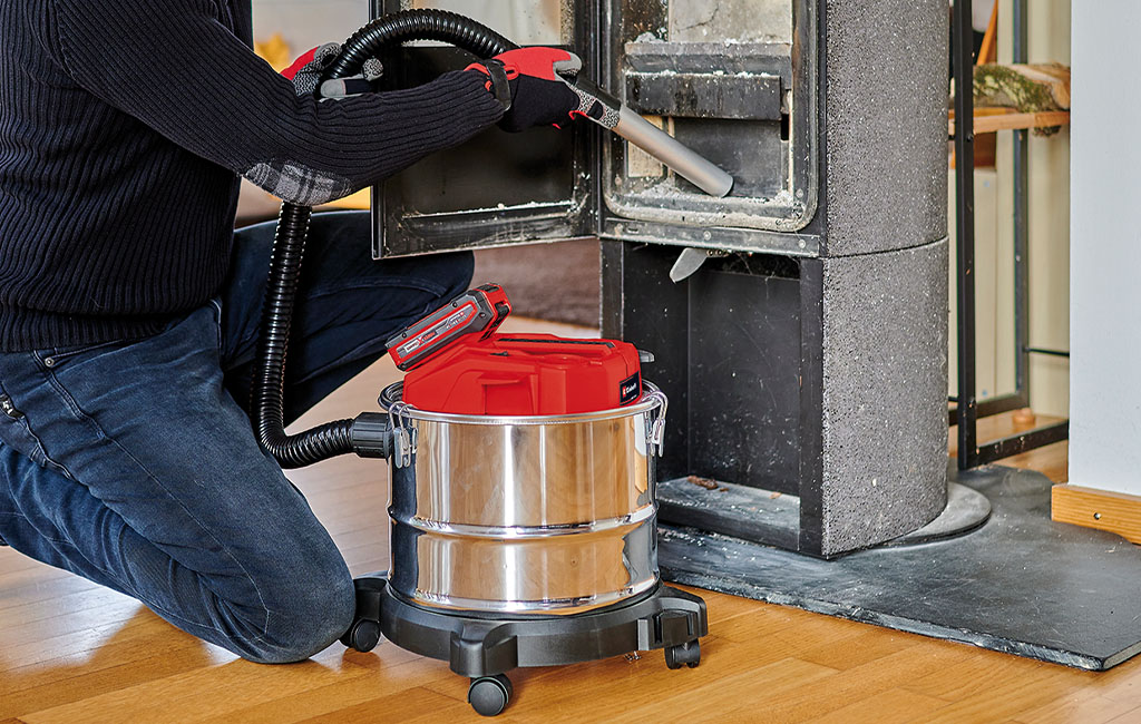 Close-up of an Einhell cordless ash vacuum in use while cleaning a wood-burning stove.