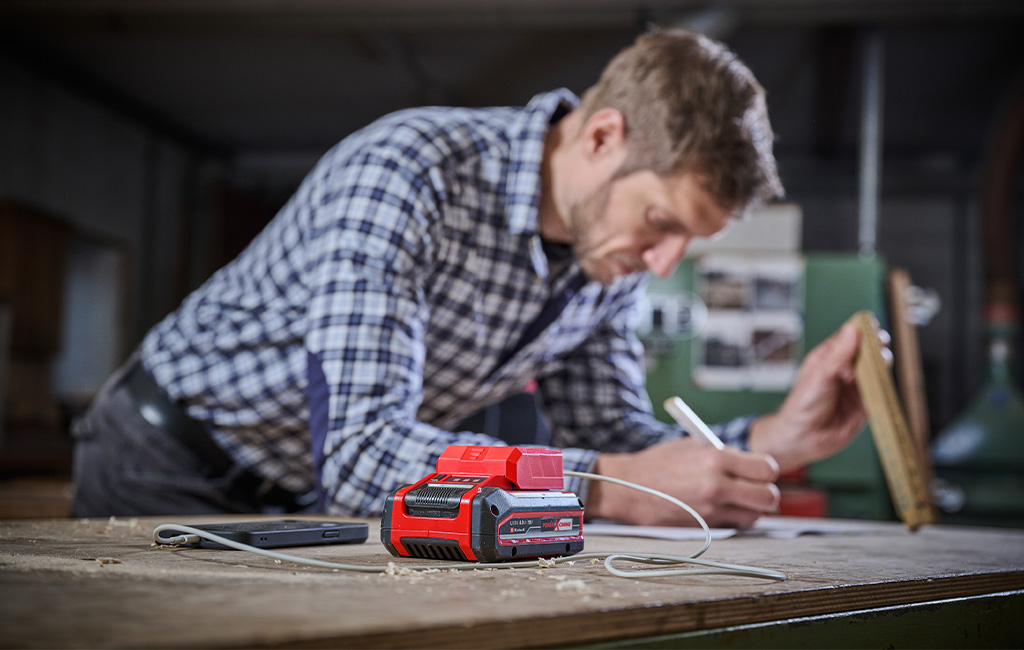 A man works at a table while a battery adapter charges his smartphone via USB.