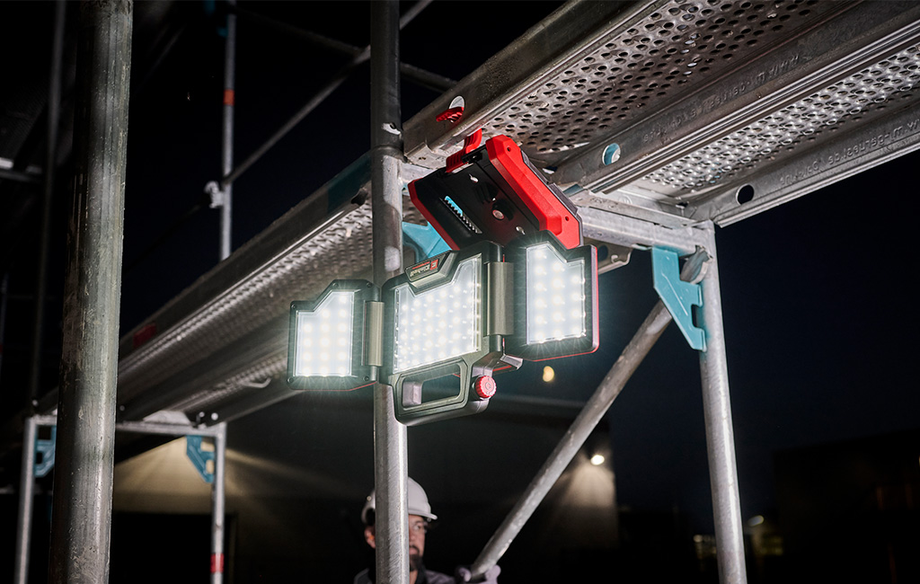 An LED work light is attached to scaffolding, illuminating a construction site at night.