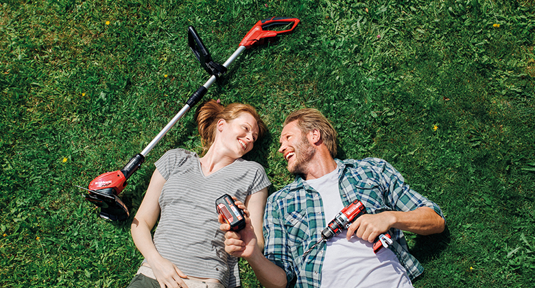 woman and man laying in the lawn with cordless lawn trimmer battery and cordless screwdriver